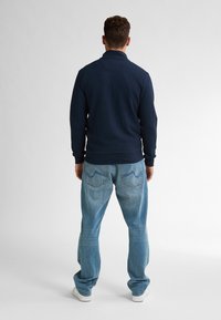 Námořnicky modrý svetr s texturou a límečkem, v kombinaci se světle modrými džíny. Oblečení má volný střih a bílé tenisky.