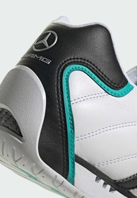 Biele a čierne kožené topánky s tyrkysovými akcentmi, so štruktúrovaným povrchom, viditeľným švom a logom Mercedes AMG.