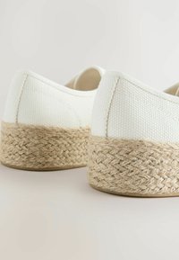 Valged kanvasjalanõud tekstuurse pealmise ja kootud jute platvormi tallaga. Kanna kõrgus on umbes 3 cm, kaunistatud õmblustega.