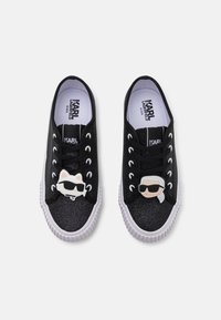 Μαύρα γκλίτερ αθλητικά παπούτσια με λευκές καουτσούκ σόλες, με πλαστικά charms σε σχήμα γάτας και γυαλιών ηλίου στα κορδόνια. Βαμβακερή επένδυση και μαξιλαρωτή σόλα.