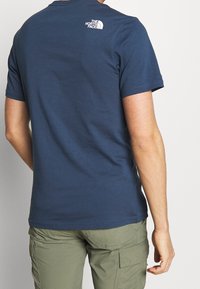 Camiseta de manga corta azul marino hecha de algodón suave; presenta un logotipo blanco en la parte superior de la espalda; combinada con pantalones cargo verdes.