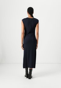 Ναυτικό μίντι φόρεμα χωρίς μανίκια με εφαρμοστό σιλουέτα, πλαϊνό σκίσιμο και λεία υφή. Συνδυασμένο με μαύρες μπούκλες με τακούνι.