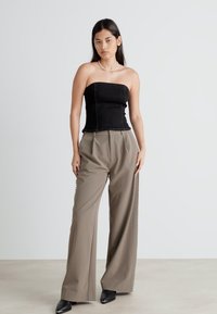 Μαύρο strapless τοπ με εφαρμοστό κορσέ, σε συνδυασμό με μπεζ παντελόνια μ wide-leg που διαθέτουν πλαινές διακοσμήσεις. Σκοτεινές παπούτσια ολοκληρώνουν την εμφάνιση.