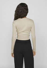 Beige langermet topp laget av myk stoff, tettsittende stil, kombinert med høyt liv svarte bukser. Glatt tekstur, enkel design, ingen synlige mønstre.