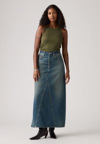 Denim maxiskjørt med høy liv, frontsplitt og falmet blå farge. Kombinert med en tettsittende olivenfarget tanktop og svarte høyhælte støvler.