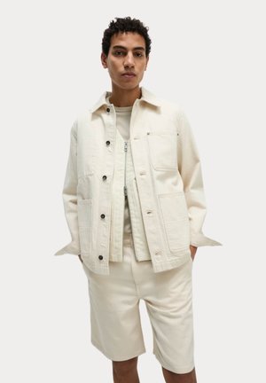 Lys beige denimjakke med knaplukning, to brystlommer og en glat tekstur, parret med matchende shorts. Casual fit.