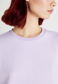 Sweatshirt crewneck lilla con scollo a coste; texture morbida e liscia; vista ravvicinata che evidenzia i dettagli del tessuto e del colore.