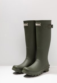 Zöld gumicsizma matt felülettel, oldalsó csatokkal és textúrált talppal a tapadás érdekében. Elöl található a "Barbour" logó.