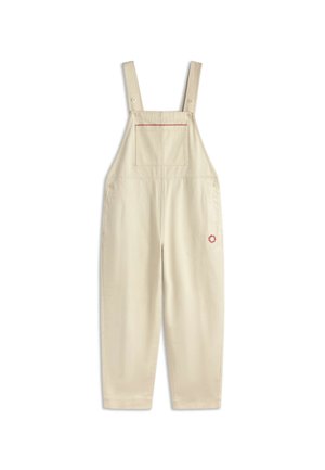 Salopette en coton beige avec bretelles réglables, poche poitrine avant avec surpiqûres rouges, et petite broderie de fleur rouge sur la jambe droite.