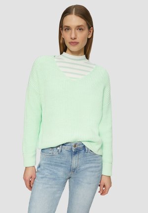 Mintgroene gebreide trui met een V-hals, oversized pasvorm, geribbelde textuur en lange mouwen, gelaagd over een wit gestreepte coltrui.
