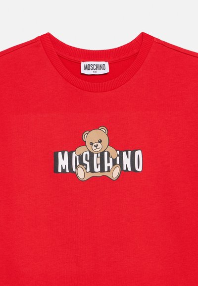 Rdeča otroška majica s kratkimi rokavi in rebrastim okroglim ovratnikom, z motivom medvedka, ki sedi na črno-belih blok črkah, ki sestavljajo napis "Moschino".