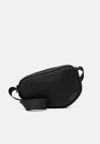 Black, zippered crossbody bag made of smooth material, featuring a flat shape, a single strap, and a small logo accent. Minimalist design.
