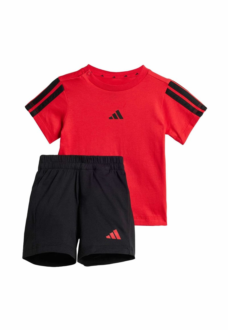 Crvena pamučna majica s crnim prugama na ramenima i logotipom, uparena s crnim kratkim hlačama koje imaju mali crveni logotip. Elastični pojas na kratkim hlačama.