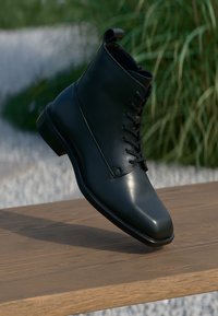 Schwarze Leder-Ankle-Boots mit spitz zulaufender Zehenpartie, Schnürung vorne und glatter Oberfläche. Robuste Sohle und minimalistisches Design.