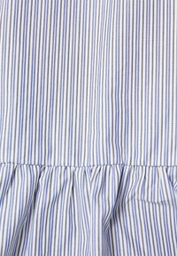 Tessuto a righe blu e bianche con linee verticali, caratterizzato da un volant arricciato nella parte inferiore. La texture appare liscia e leggera.