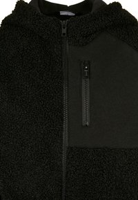 Schwarze Zip-Jacke mit weichem, flauschigem Fleece-Material auf der einen Seite und einem glatten, matten Stoff auf der anderen Seite, ausgestattet mit einem Reißverschluss an der Vorderseite.