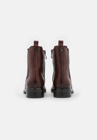 Bottes chelsea en cuir marron avec une texture lisse, fermeture éclair à l'arrière, boucles de traction, et un petit talon carré.