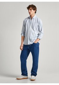 Chemise à rayures bleu clair et blanche avec des manches longues, associée à un jean bleu ample et des baskets blanches. Comprend une poche sur la poitrine.