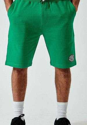 Shorts de sport verts avec taille élastique et cordon de serrage. Comprend une poche latérale et un patch logo rond sur la jambe droite.