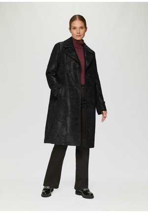 Black textured overcoat with a wide collar, featuring an embossed leaf pattern, worn over a dark turtleneck and black trousers. Glossy shoes.