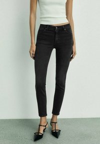 Black skinny jeans with a high waist, featuring five pockets, a button closure, and slight distressing. Paired with black pointed-toe flats.