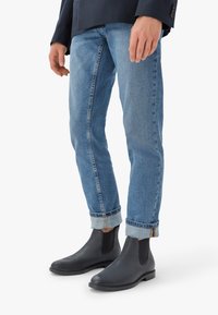 Melni ādas čelija zābaki ar elastīgām sānu paneļiem, apvienoti ar gaiši zilu džinsu biksēm ar sarullētām piedurknēm un vieglu izbalējumu.