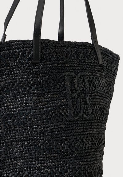 Sac cabas tressé noir avec des poignées en cuir et un monogramme tressé texturé sur le devant, sur un fond uni.