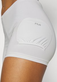 Hvite treningsshorts laget av stretchy stoff med en rynket detalj på sidelommen. Inkluderer Fila-logo i sølv.