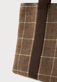 Καφέ τσάντα ώμου από μάλλινο ύφασμα με μπεζ και κόκκινο καρό σχέδιο και φαρδύ σκούρο καφέ λουρί σε λευκό φόντο.