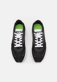 Baskets noires et grises en matériau mesh et daim, avec des lacets blancs, des semelles intérieures rembourrées vertes et des accents de semelle blanche contrastants.