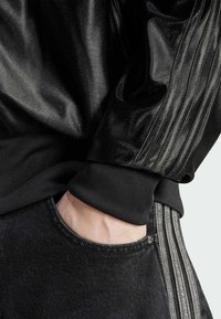 Svart satinjacka med ribbat mönster vid ärmsluten, i kombination med mörka denimbyxor som har sidoficka och ljusgrå ränder.
