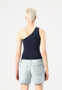 Marineblå, en-skulder topp laget av elastisk materiale, kombinert med lyseblå denimshorts med frynsete nederkant og baklommer.