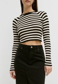 Pull cropped à rayures noires et blanches avec une texture côtelée et des manches longues, associé à une jupe en denim noire taille haute.
