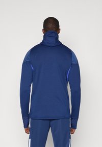 Navy niebieska bluza sportowa z wysokim kołnierzem i długimi rękawami, z kontrastowym materiałem na ramionach, gładką teksturą i dopasowanym krojem.