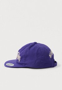 Gorra de béisbol ajustable morada con texto bordado beige en la parte delantera y lateral, visera plana y etiqueta de marca en la visera.