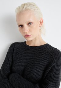 Pull à côtes gris foncé avec un col rond et des manches raglan. Le matériau a l'air doux et texturé. Le mannequin a les cheveux courts et de couleur claire.