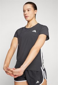Svart atletisk T-skjorte med korte ermer, med perforert tekstur og hvite logo-detalljer, kombinert med svarte shorts med kontrasterende side-striper.
