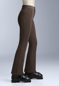 Hnědé rozšířené kalhoty vyrobené z hladké a flexibilní tkaniny. Obsahují švy podél stran a zipový uz�ávěr v pase. Nosené s černými botami.