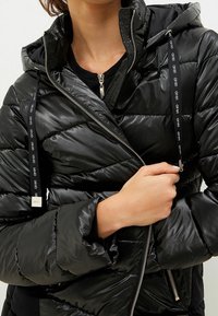 Czarna kurtka puchowa o błyszczącej, pikowanej fakturze, z kapturem, z przodu na zamek błyskawiczny i czarnymi sznurkami ściągającymi z akcentami logo.
