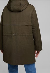 Parka de color verde oliva con capucha, que presenta un corte recto, bolsillos con solapa y cintura con cordón ajustable. Textura de tela mate.