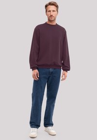 Burgundy sweatshirt with a round neck, relaxed fit, and ribbed cuffs, paired with blue straight-leg jeans and white sneakers.