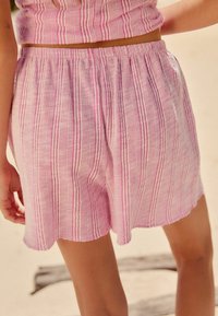 Shorts roses en tissu léger présentant des rayures verticales en rose plus foncé, avec un ourlet effiloché et une taille élastique.