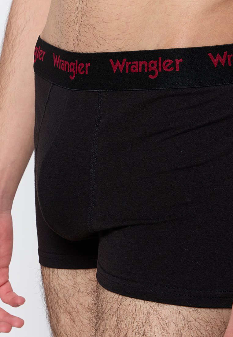 Zbliżenie na męski tors w czarnych bokserkach z czarnym pasem z czerwonymi logo "Wrangler".