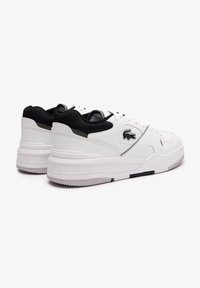 Hvite lær-sneakers med svarte mesh-detaljer. Kraftig såle, teksturert mønster på yttersålen, og en subtil logo detalj på siden.