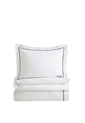 White pillow and folded duvet with thin dark piping along edges, pillow embroidered with small brand name in corner.