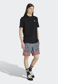 Sort t-shirt med korte ærmer og hvidt logo, parret med grå shorts med leopardprint og røde striber, sorte sokker og sorte sneakers.