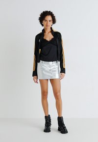Black zip-up jacket with yellow stripes, black camisole, silver mini skirt, and black lace-up boots. Smooth materials and form-fitting style.