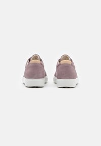 Zapatillas de ante púrpura con suelas de goma blanca, que presentan una forma redondeada, un diseño minimalista y una textura suave. La vista trasera muestra detalles en cuero suave.