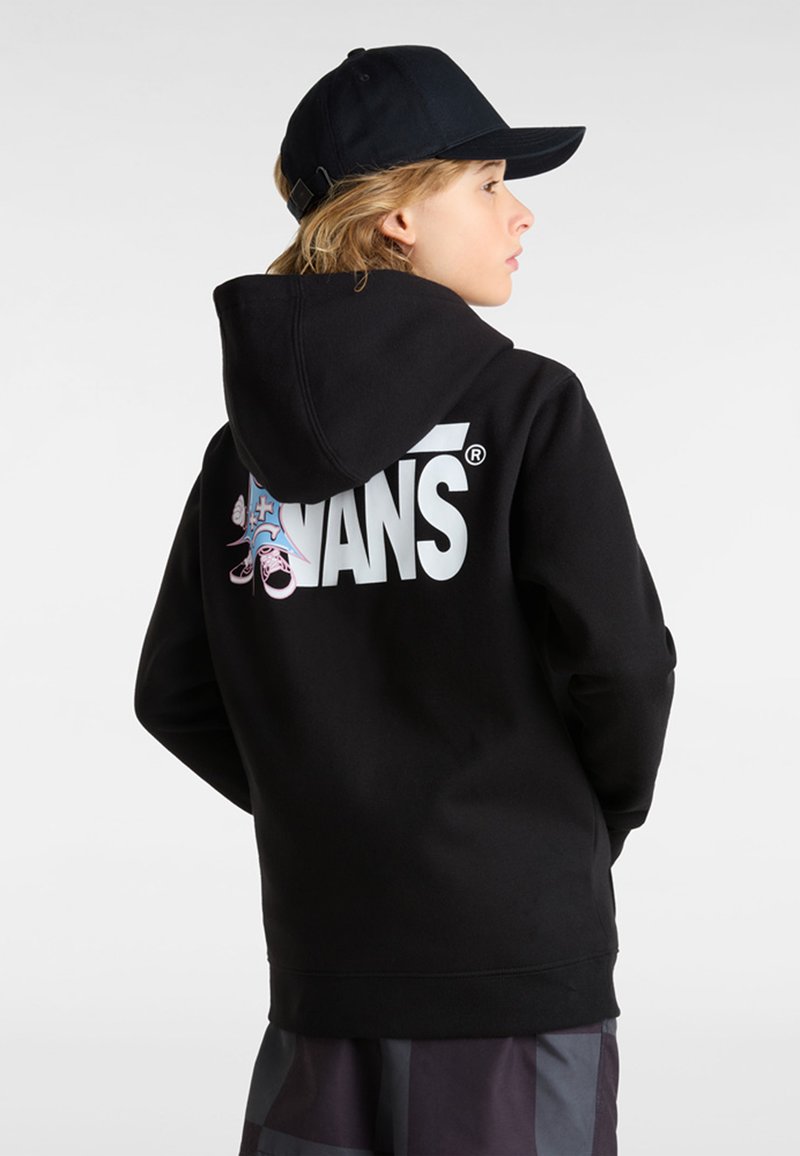 Hoodie noir avec un grand logo blanc Vans et des accents graphiques au dos. Comprend une capuche et des poignets côtelés. Porté avec une casquette noire.