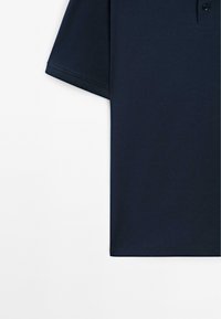 Námořnická polo košile s límečkem, krátkými rukávy a páskem se třemi knoflíky. Tkanina vypadá hladce s jednoduchým, jednobarevným designem.